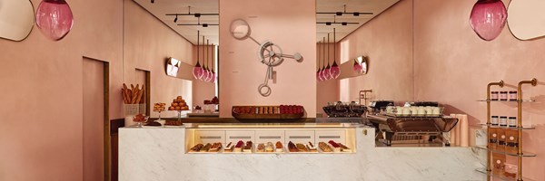 A chic patisserie interior with pink walls, a marble counter, and a central wall clock, showcasing a selection of pastries beneath glass.