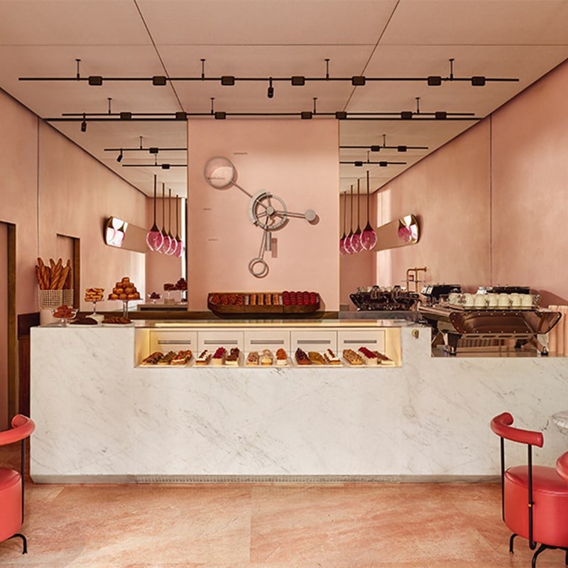 Full view of the patisserie’s interior, featuring a marble-fronted counter, mirrored walls, and modern pink seating.