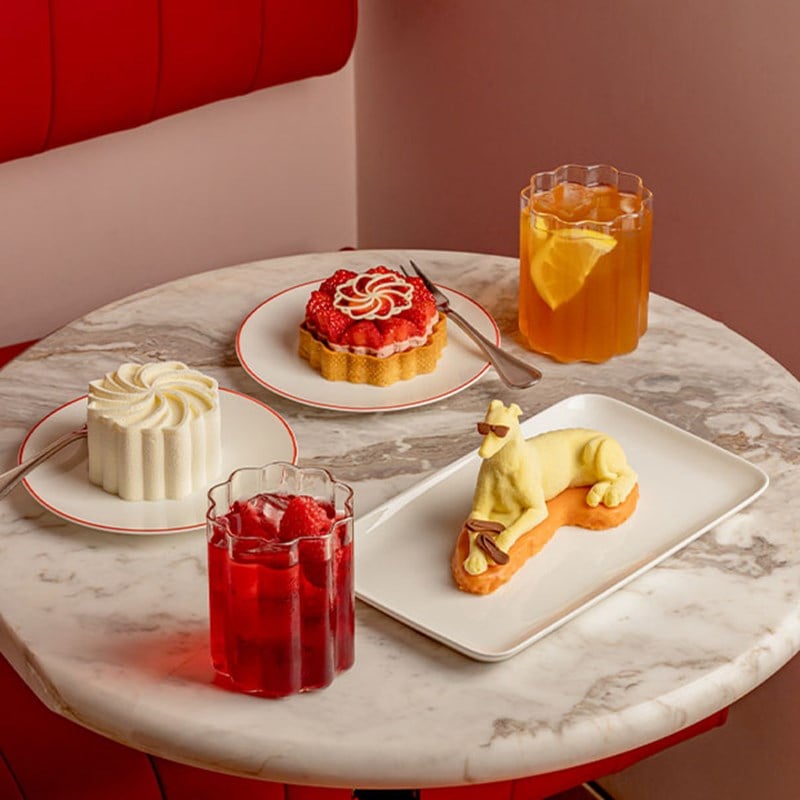 A close-up of an intricately sculpted white mousse cake with a velvety texture, served on a white plate with red trim and accompanied by a dessert fork.