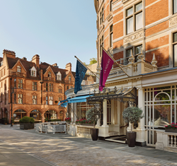 Exterior view of The Connaught Hotel in Mayfair, with ornate signage, potted trees, and the red brick Moynat storefront opposite.