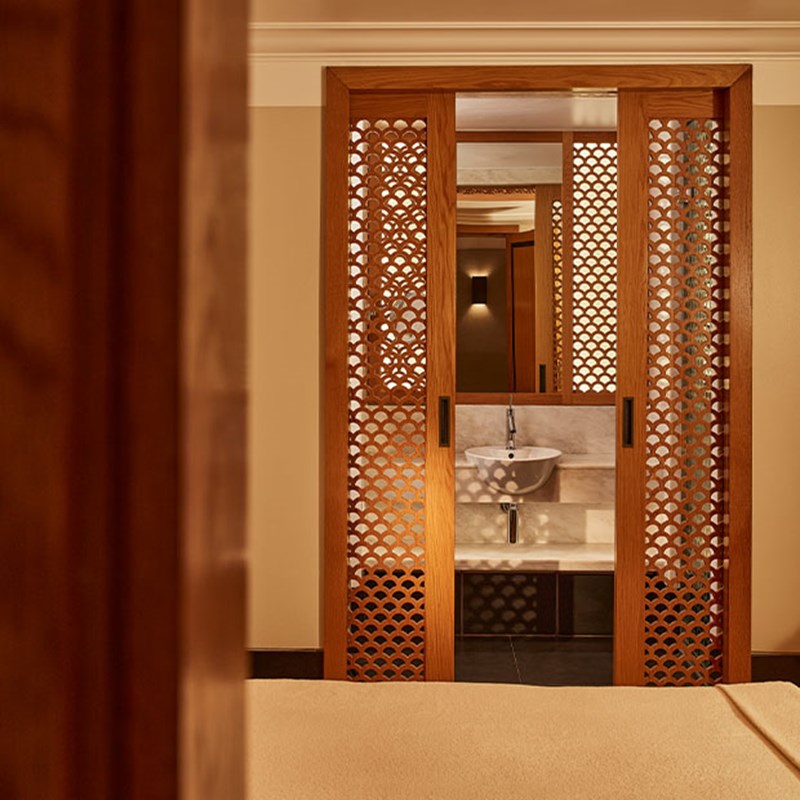 Close-up view of a marble sink behind decorative wooden lattice sliding doors, framed by warm beige and wood-toned interiors.
