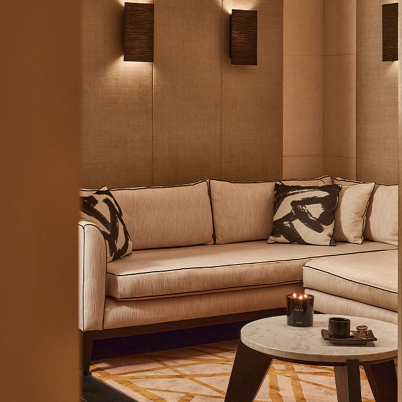 Cosy, neutral-toned lounge with plush sofas, black-and-white patterned cushions, soft lighting, and a round marble-topped coffee table with candles.
