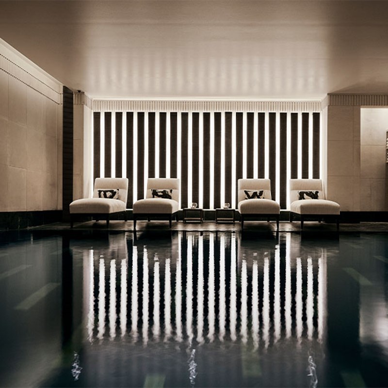 Refined spa space featuring modern loungers and black-and-white striped wall panels, reflected in the still surface of the pool.