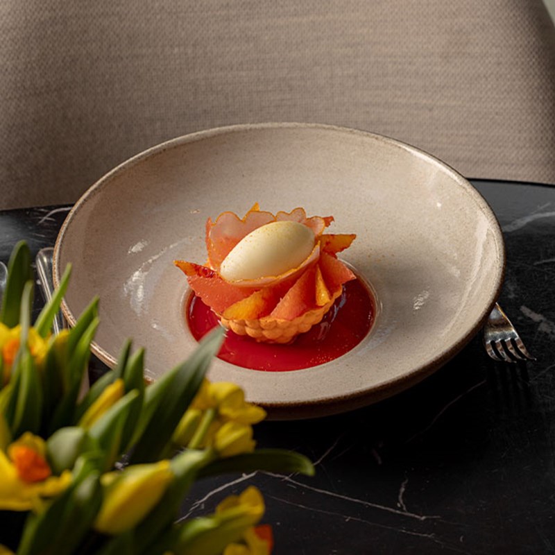 Artistic dessert of sliced citrus and sorbet presented in a pastry shell atop bright red coulis in a ceramic bowl.