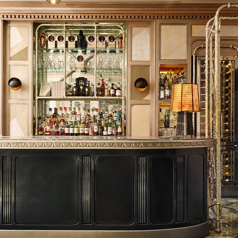 Stylish cocktail bar with mirrored shelving, an array of spirits, a vintage black counter, and warm ambient lighting from a lamp.