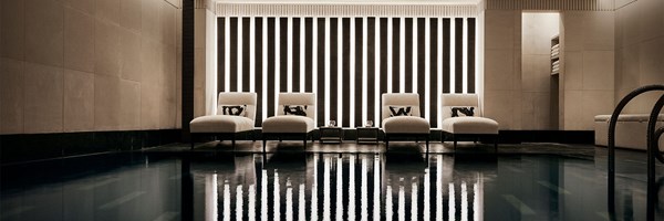 Tranquil indoor pool with modern striped lighting and four cream loungers, reflected perfectly in the water’s still surface.