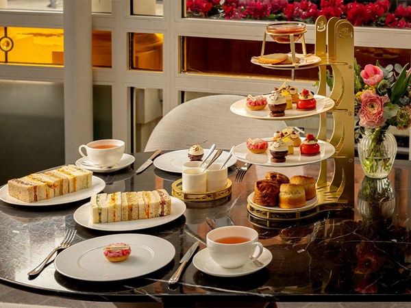 Classic afternoon tea at The Connaught, with a three-tier stand of delicate pastries, finger sandwiches, scones, and two cups of tea, set by a bright window.