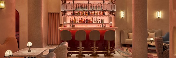 A view of the Red Room bar. 4 bar stools are tucked behind a pink onyx bar, with shelves of spirits lit up behind it.
