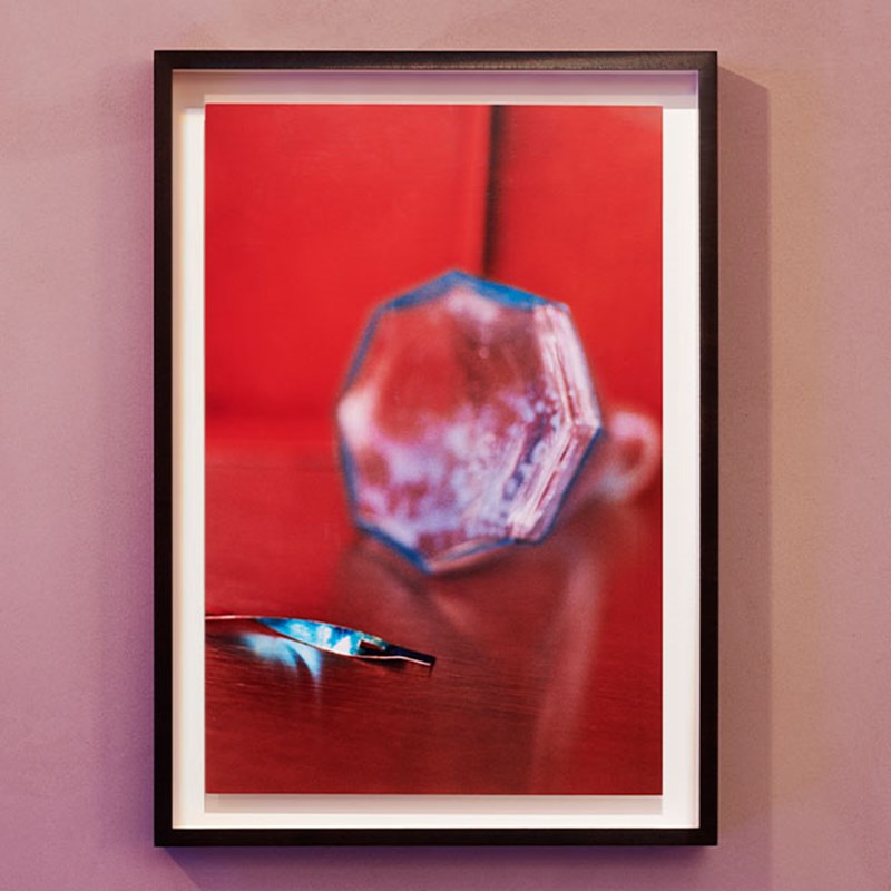 Red abstract painting with a white outline and hung on the wall in a black frame.