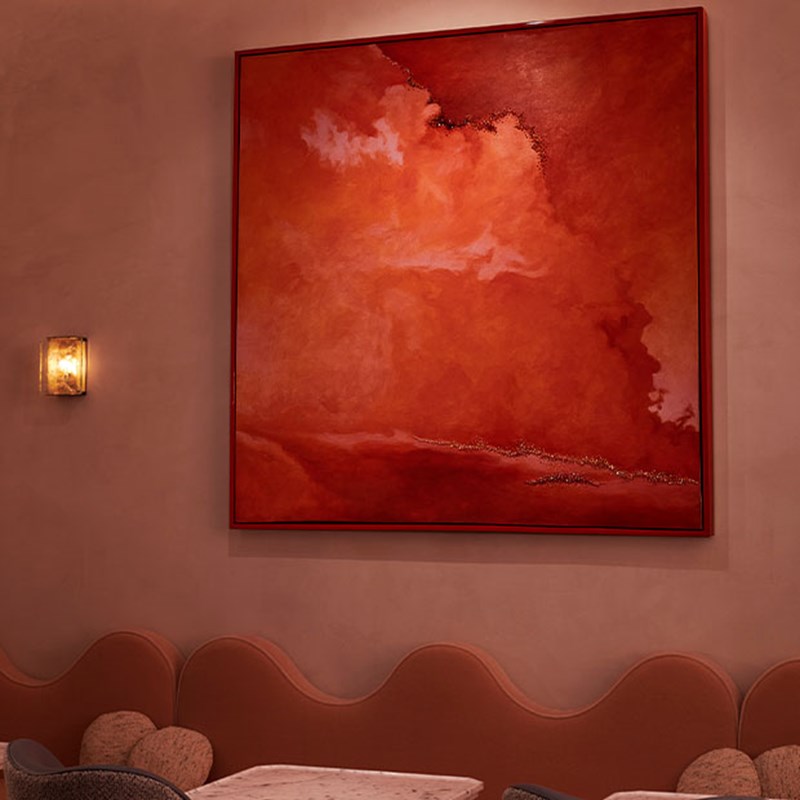 Abstract painting comprising of varying colours of red, hung on the wall in a thin red frame.