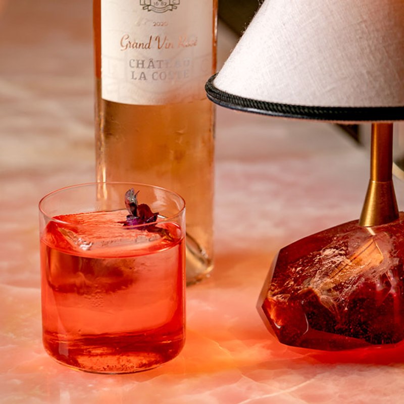 Red cocktail in a small glass, with a bottle of rose wine behind it.