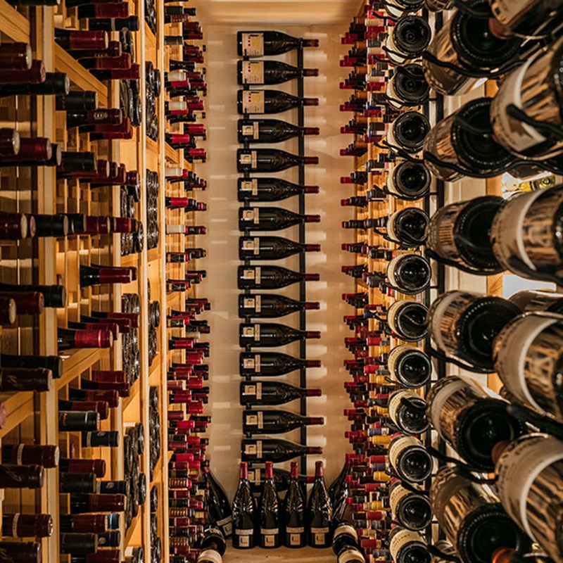 Wine cellar with lots of wine bottles in wine racks, and lined up on the floror.