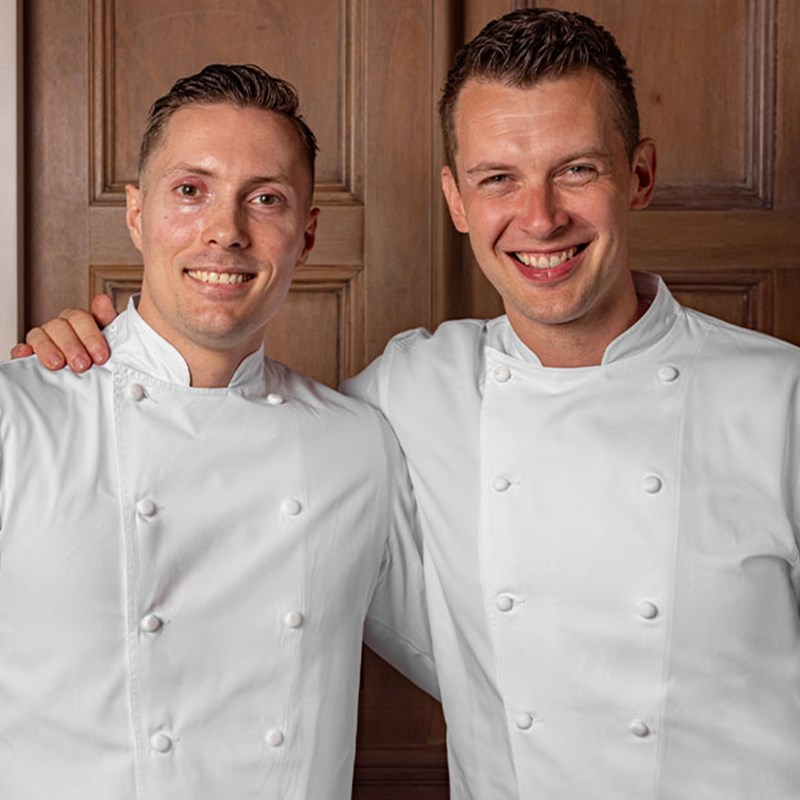 Two Helene Darroze chefs, smiling next to each other in their chef whites.