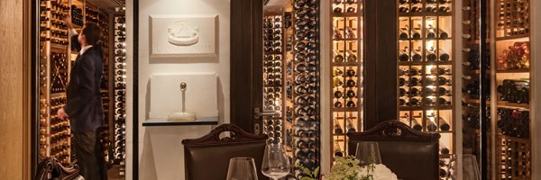 Private dining room with atable laid with white table clot, vase of flowers and wine walls. A man reaches up to select a bottle.
