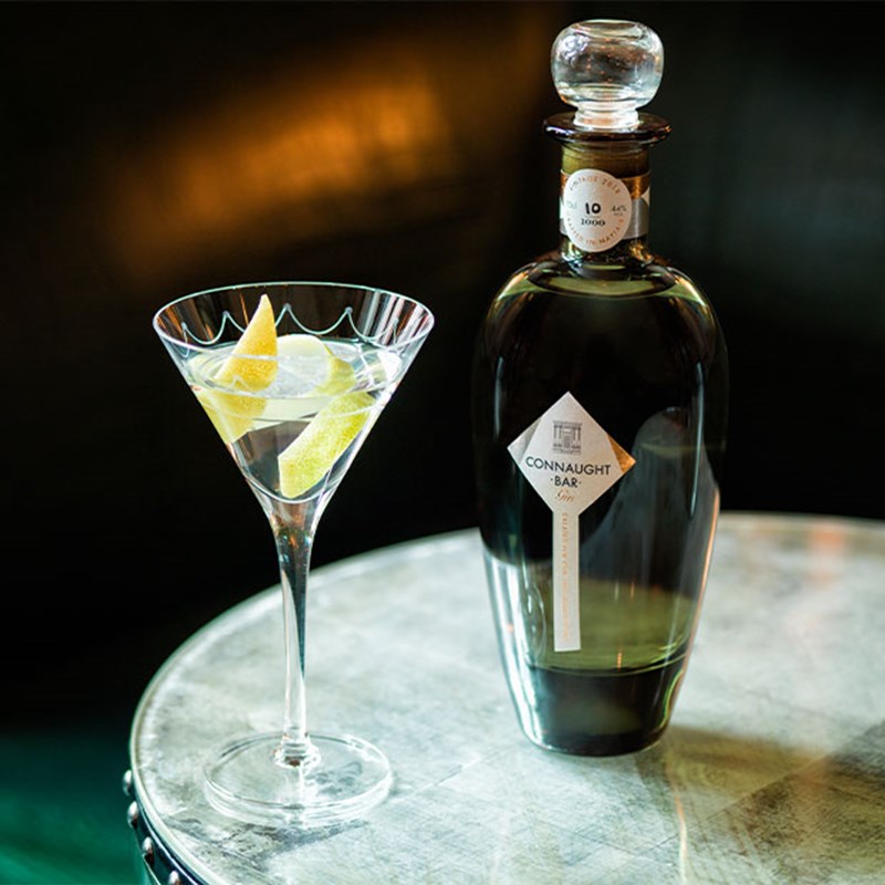 martini glass with lemon peel next to a green bottle of gin