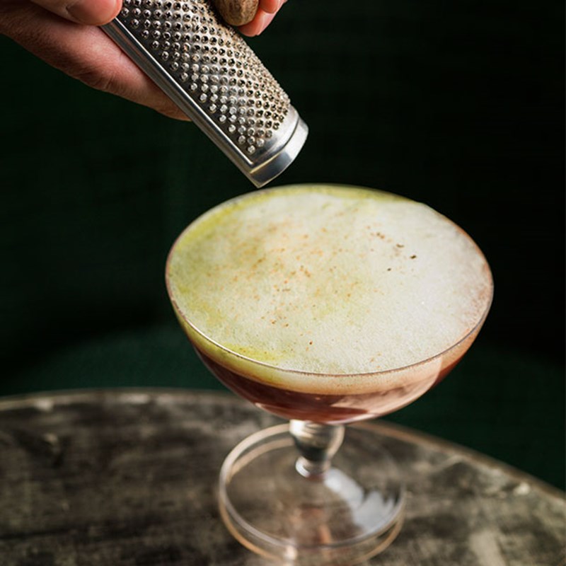 cocktail garnish being grated onto cocktail