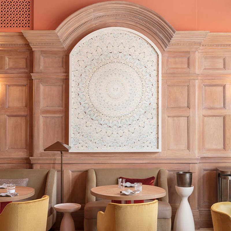 A serene dining area with pale wood panelling, curved banquettes, and a large mandala-style artwork framed within a softly arched wall niche.