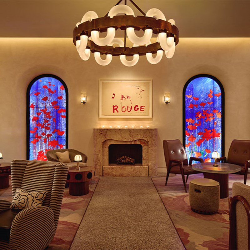 A luxurious lounge with sculptural armchairs and warm lighting, featuring vibrant stained glass windows, a fireplace, and framed art reading