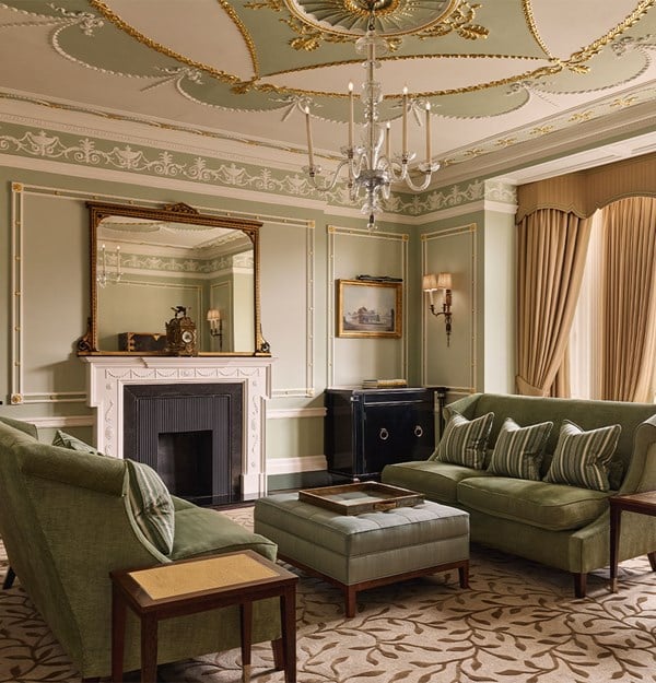 Elegant sitting room with pale green walls, gold detailing, and a crystal chandelier, featuring plush green sofas, a marble fireplace, and classic décor accents.