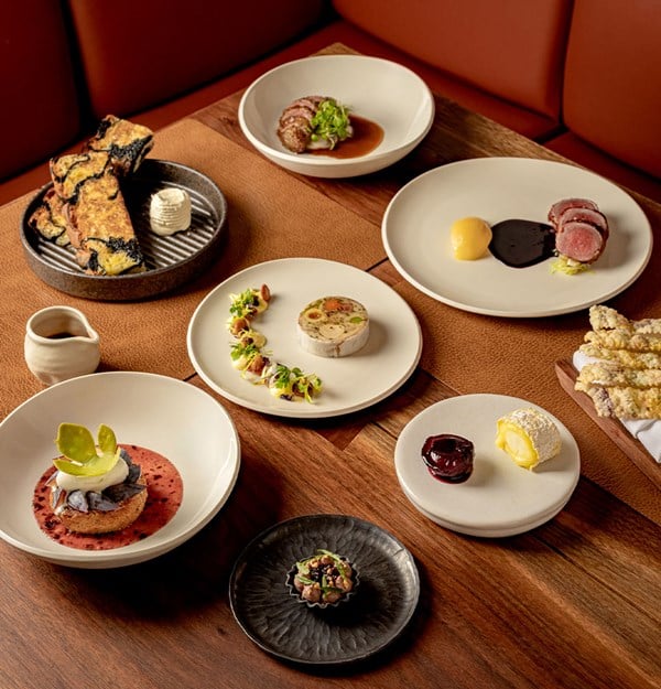 Assorted fine dining dishes artistically presented on a wooden table, including meats, terrines, desserts, and breads, showcasing contemporary British cuisine.