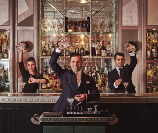 Three mixologists preparing drinks at The Connaught Bar, surrounded by the timeless elegance of the interior.