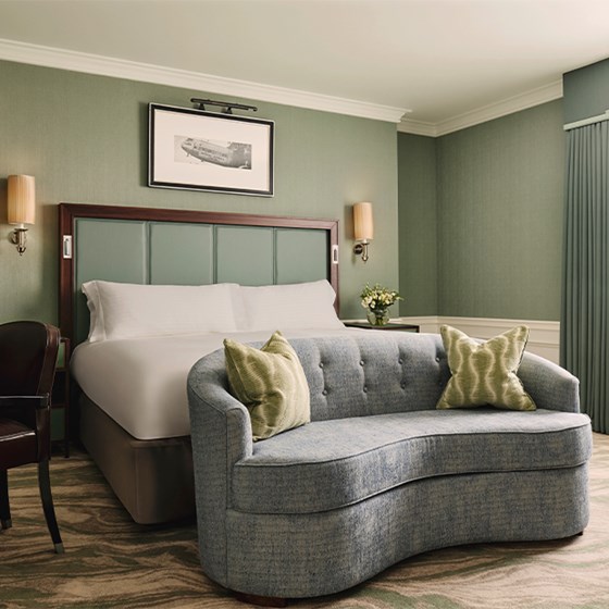 A serene and stylish guest room featuring a plush bed, a curved sofa, and calming green tones, exuding timeless elegance.