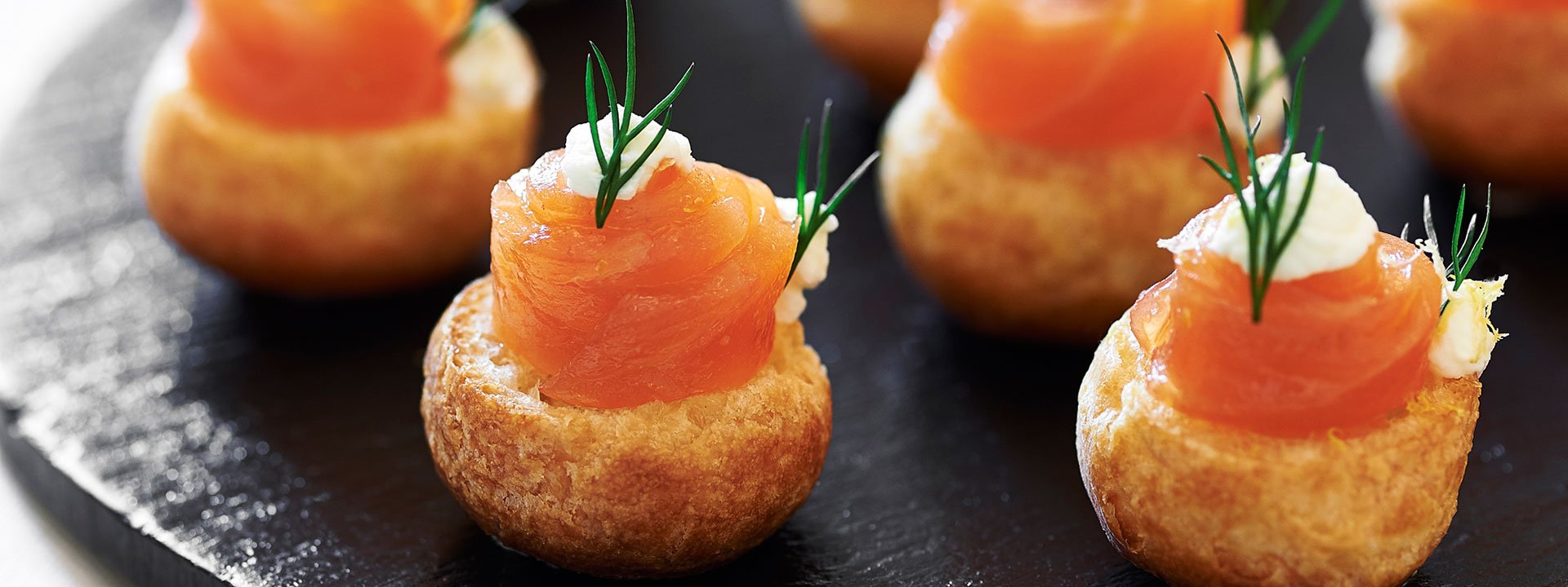 A black plate with canapes with a green twig for decoration.