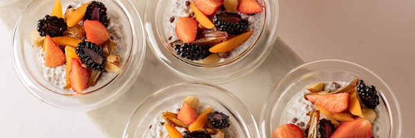 Bowls of chia seed pudding topped with fresh strawberries, blackberries, apricots, dates, and nuts, served in clear glass dishes.