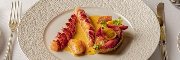 Fine dining plate with lobster tail medallions in a golden sauce, served alongside heirloom tomato bruschetta with microgreens.