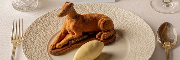 Dessert shaped like a reclining dog with a chocolate base, paired with a scoop of vanilla ice cream on a fine dining plate.