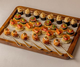 Wooden tray of assorted gourmet canapés, including salmon with caviar, tuna with herbs, crab, and fruit garnishes, each neatly arranged in rows.