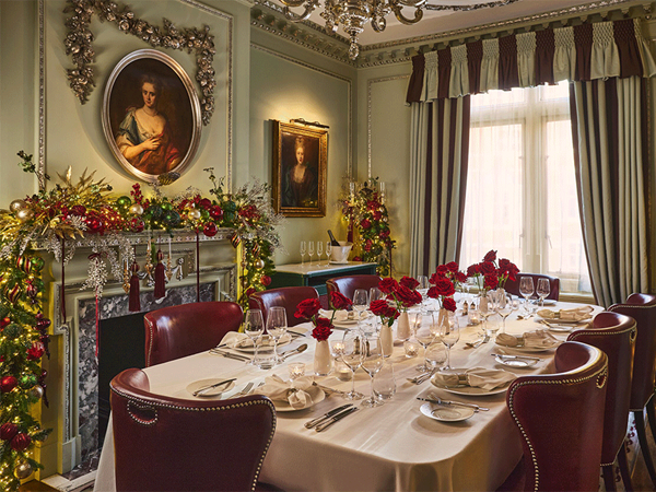 A decorated Georgian dining room with a festive garlanded fireplace and a long table set with red roses.