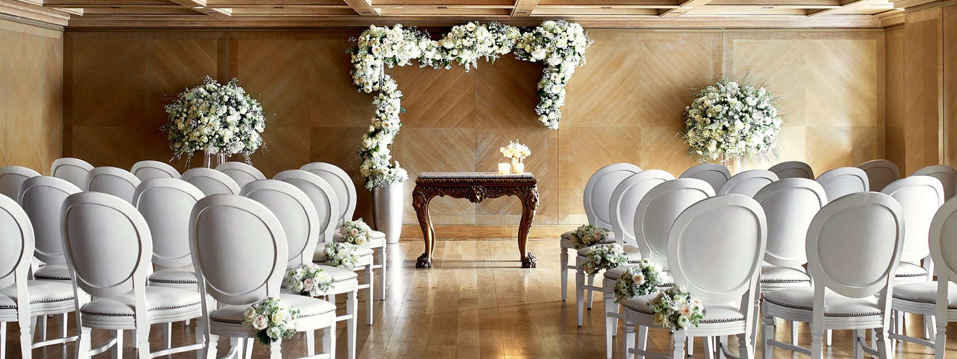 View of the setting for the wedding ceremony in the Maple Room at The Connaught, decorated with floral arrangements.