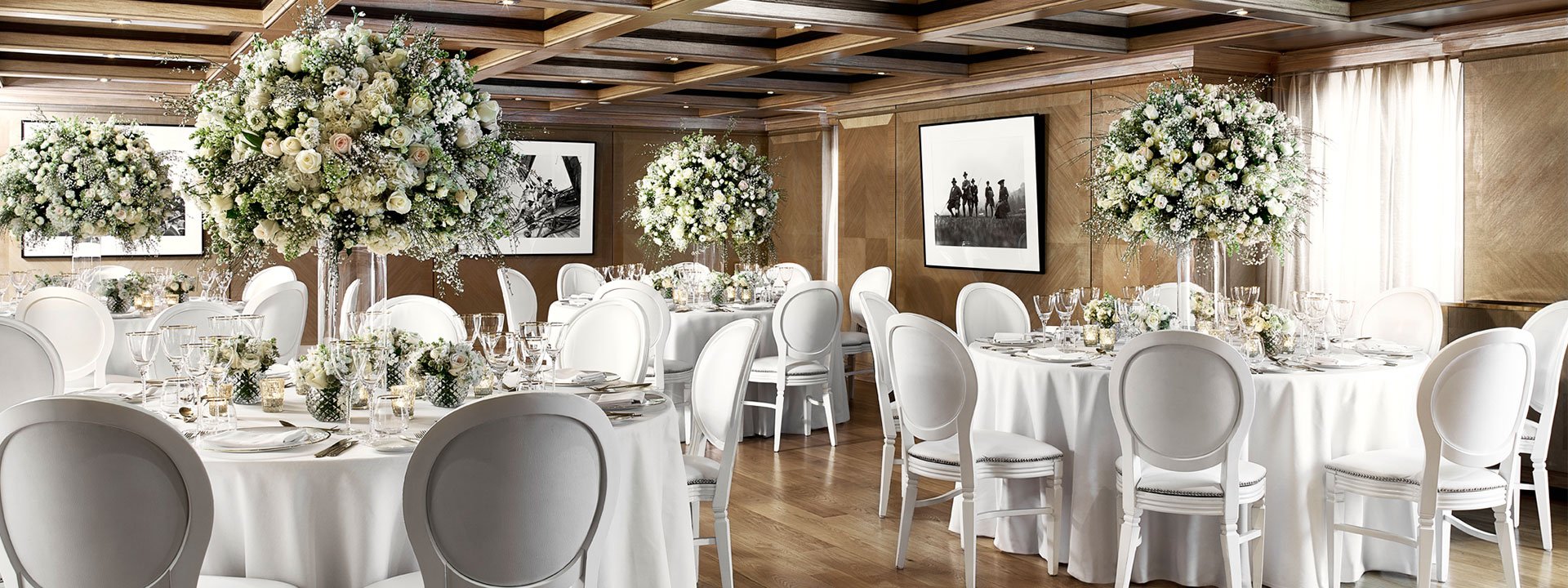 View of dining tables decorated with floral arrangements for a wedding ceremony in the Maple Room at The Connaught.