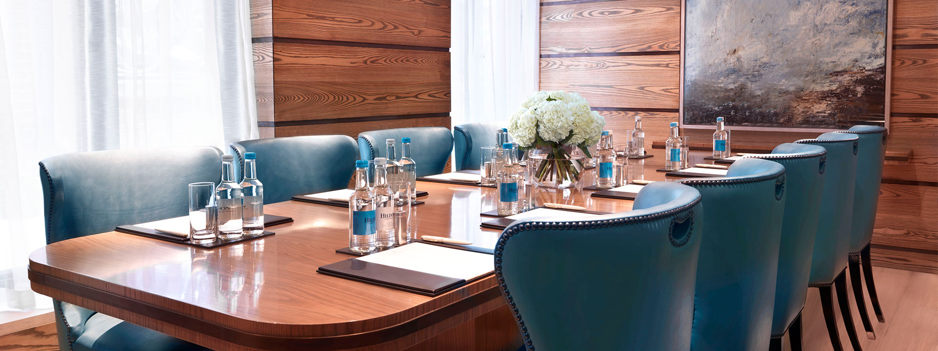 A long wooden table with glasses of water, and blue seats.