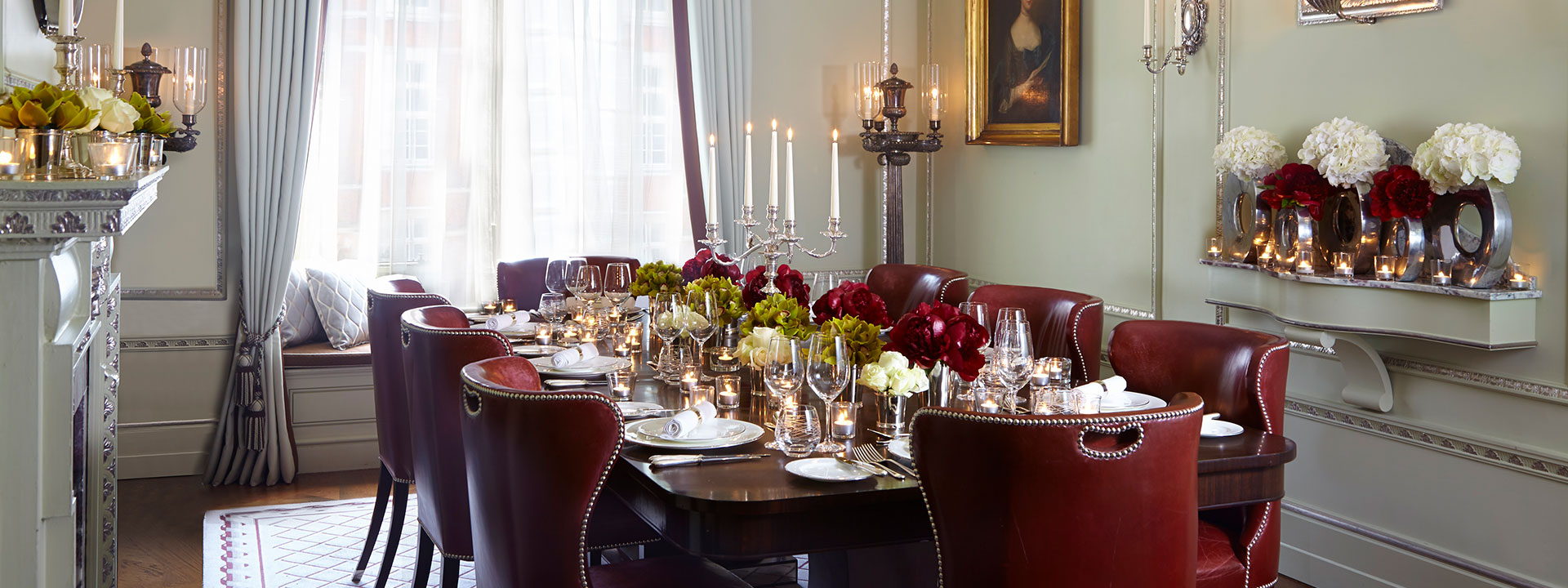 Long table with fine cutlery, long candles and red seats next to a large window at the Georgian Room.