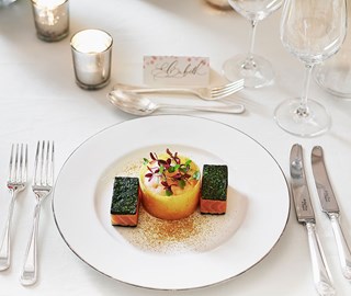 Presentation of a delicious salmon dish on a white plate, with escaige and candles at The Connaught.