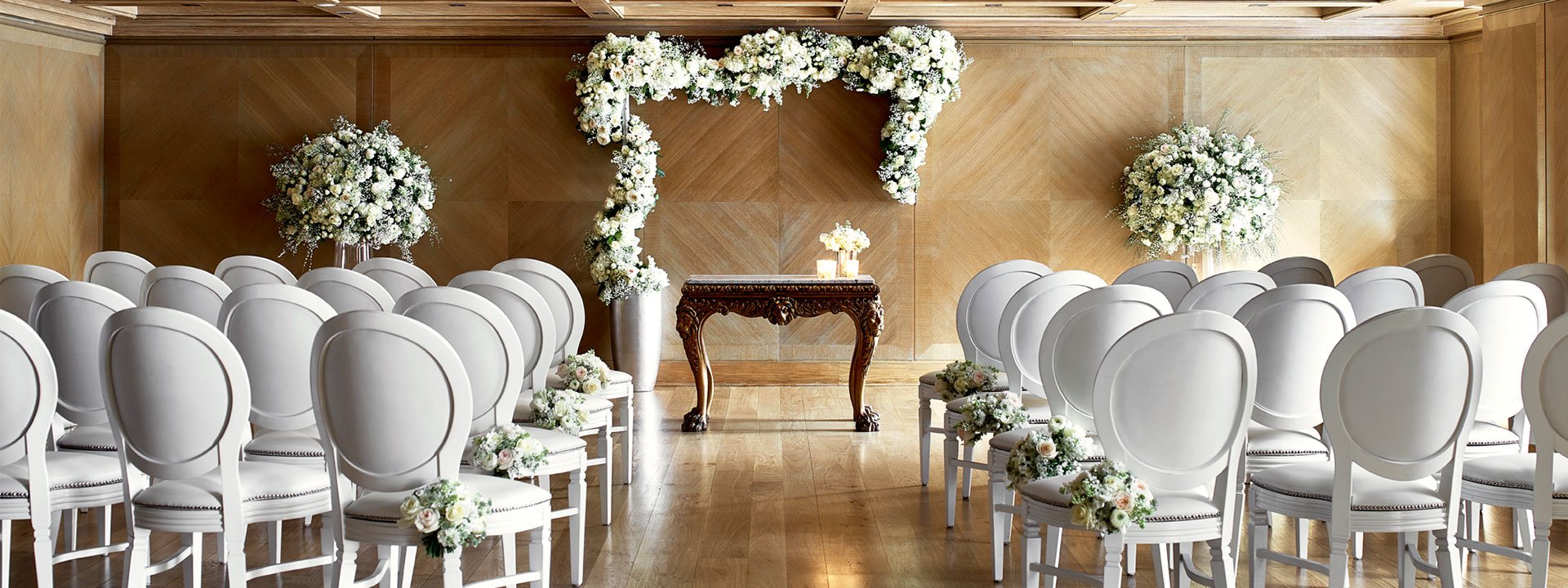 View of the setting for the wedding ceremony in the Maple Room at The Connaught, decorated with floral arrangements.