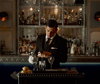 A depiction of a sophisticated bartender making a cocktail at the bar at The Connaught.