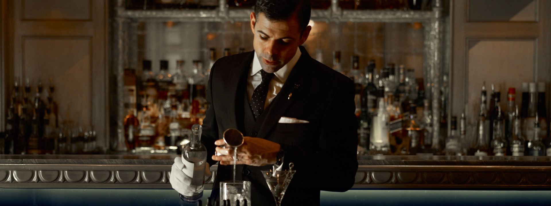 A depiction of a sophisticated bartender making a cocktail at the bar at The Connaught.