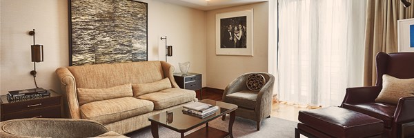 Softly lit bedroom with a velvet curved sofa, round table and tall windows with sheer and beige curtains.