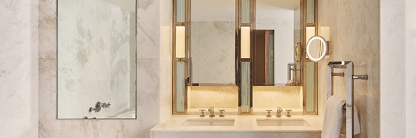Bright marble bathroom with double sinks, mirrored cabinets and warm lighting.