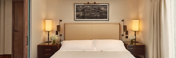 Calm bedroom with a padded headboard, bedside lamps and framed artwork above crisp white bedding.