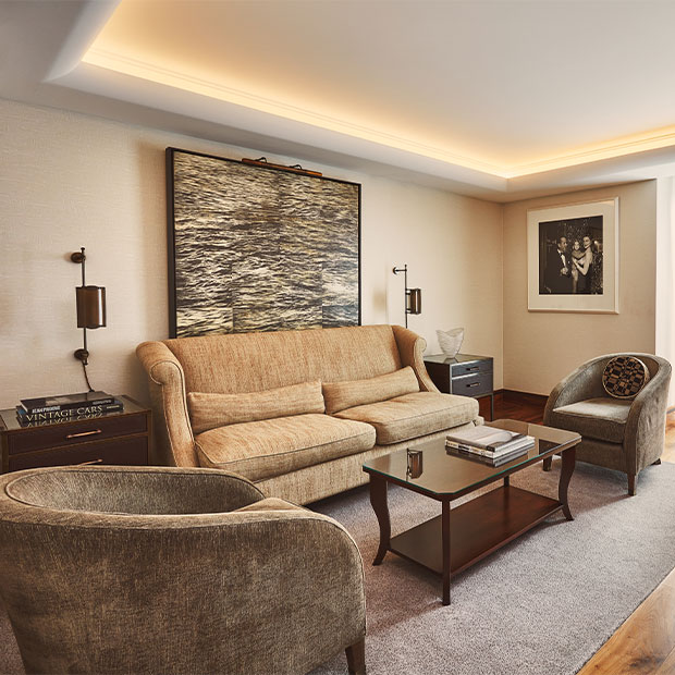 Elegant living room with a tan sofa, armchairs and glass coffee table beneath large framed artwork.