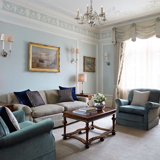 Comfortable beige and green armchairs and sofa, with artwork on the walls in the Carlos Suite.