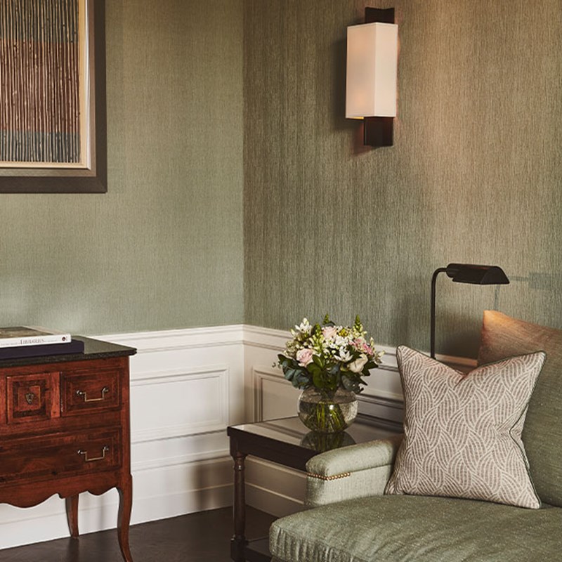 View of corner of the suite, with a bit of te green sofa in view, and on the left there is a small table with a vase of flowers.