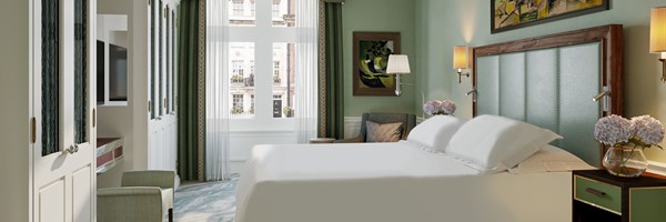Coburg suite. Bedroom with double bed made up with white bedding, 2 green bed side tables on either side, a green headboard, green walls, green curtains and a view outside the window of a residential London street.
