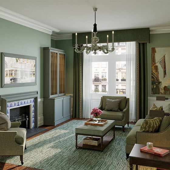Coburg Suite: green toned sofa, and 2 arm chairs around a coffee table with a vase of pink flowers sitting on top a fire place with blue tiles and a window at the back overlooking a residential London street.