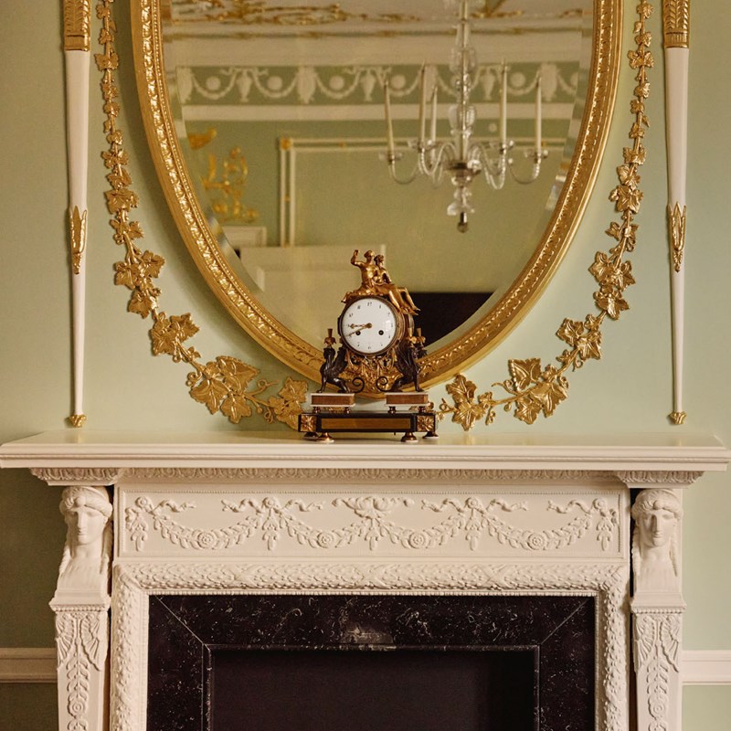 Neoclassical marble fireplace in Suite 205 at The Connaught, framed by an ornate gold mirror and flanked by delicately carved motifs.