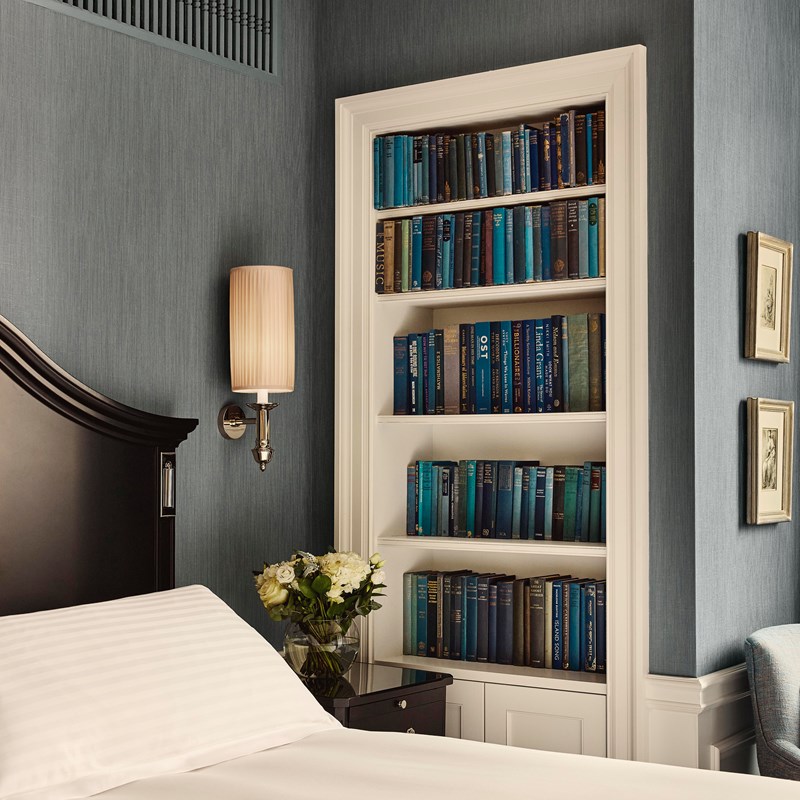 Bookshelf alcove in a Suite 205 bedroom, with a curated library of blue-hued books and soft textured wallpaper in deep teal.